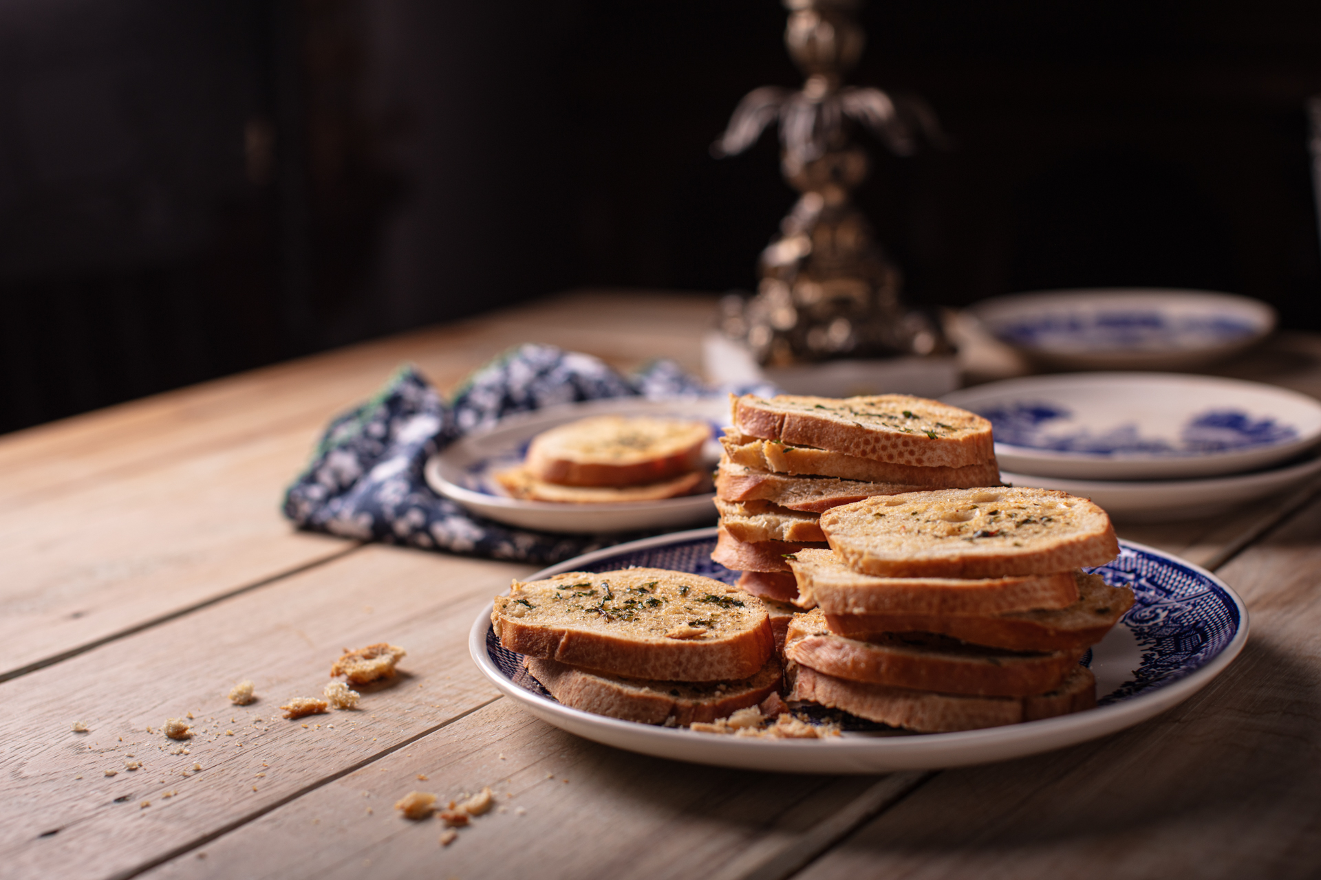 Crab boil crostini on a blue and white plate with other blue and white saucers in the background. All of this is resting on a natural wood colored tabletop. A gold candlestick is in the background.