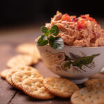 pimento and cheese dip in a floral bowl surrounded by crackers on a wooden background