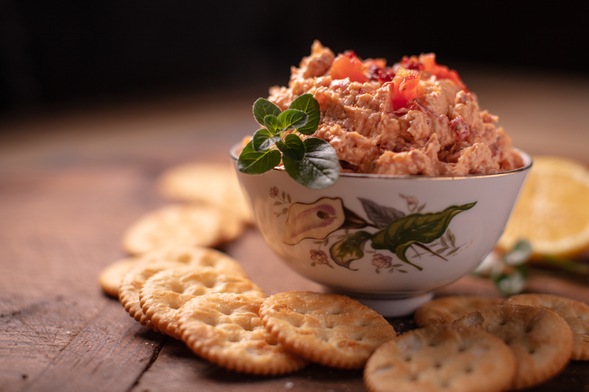 pimento and cheese dip in a floral bowl surrounded by crackers on a wooden background