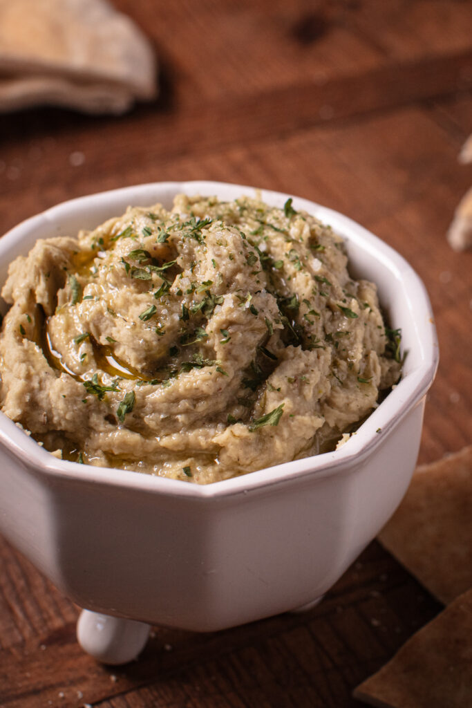 butterbean and pistachio hummus in a white footed bowl on a wooden background
